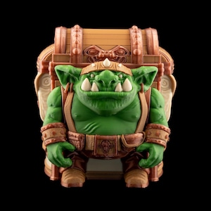 May include: A green goblin figure with large white teeth, wearing a brown belt, boots, and armbands. The goblin is carrying a treasure chest on its back. The chest is brown with copper-colored accents. The background is black.