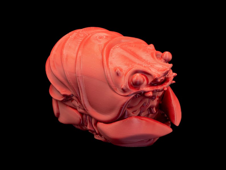 K&ouml;nnte beinhalten: Korallenfarbene, 3D-gedruckte Skulptur einer Kreatur mit segmentiertem K&ouml;rper, gro&szlig;en Augen und einem bedrohlichen Maul. Die detaillierte, strukturierte Oberfl&auml;che ist vor schwarzem Hintergrund. Das Design erinnert an einen Krebs oder ein Insekt.