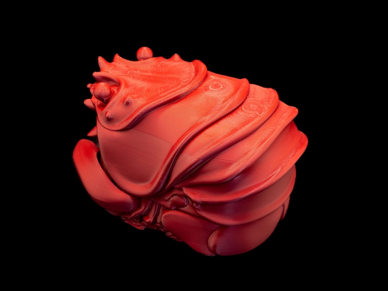 K&ouml;nnte beinhalten: Eine leuchtend rote, abstrakte Skulptur mit einem geschichteten, muschelartigen Design. Das Kunstwerk hat eine glatte, gl&auml;nzende Oberfl&auml;che und ist vor einem tiefschwarzen Hintergrund platziert, der seine Form und Textur hervorhebt. Das St&uuml;ck erinnert an organische Formen.