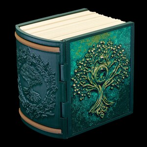 May include: A green book with a gold embossed tree design on the cover. The book is closed and has a decorative wooden spine.