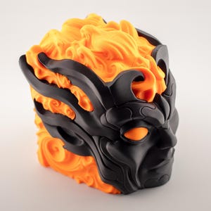 May include: A 3D-printed sculpture of a stylized face with a fiery design. The face is black with orange accents, including the eyes and a flame-like top. The sculpture has a detailed, textured surface.