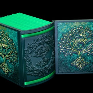 May include: A green and gold decorative box with a tree of life design. The box is open and the lid is propped up. The box is made of wood and has a textured finish.