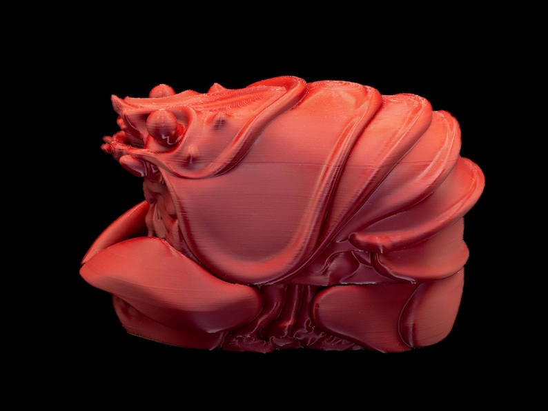 K&ouml;nnte beinhalten: Eine rot gef&auml;rbte 3D-Skulptur einer abstrakten Form, m&ouml;glicherweise einer Krabbe oder einem Krebs, vor schwarzem Hintergrund. Das Objekt hat eine strukturierte Oberfl&auml;che mit geschichteten, gebogenen Elementen.