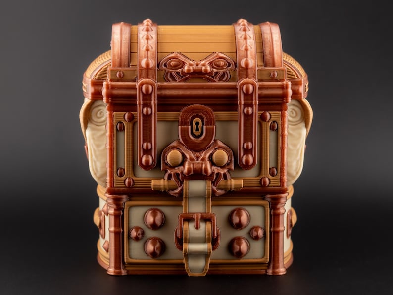 May include: A decorative treasure chest in shades of brown, beige, and copper. The chest features intricate details, including a keyhole, decorative rivets, and a clasp. The design has a vintage or fantasy theme.