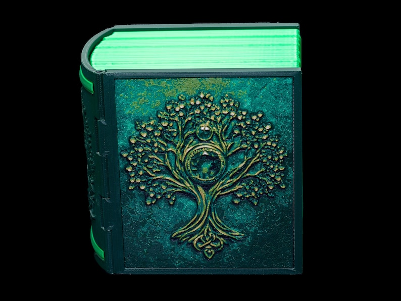 May include: A teal green book with a gold embossed tree design on the cover. The book is closed and the pages are visible, glowing green.