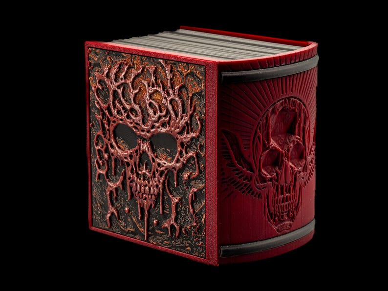 The book of the dead is blood red and has a skull engraving. The heavy metal color is paired with black pages and bindings. The binding features a skull with D20 eyes and haunting angel wings.
