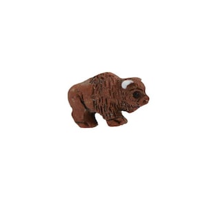 Op de afbeelding: Een klein, bruin keramiek beeldje van een bizon met witte hoorns. Het beeldje staat op een witte achtergrond.