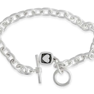 Könnte beinhalten: Ein silbernes Kettenarmband mit einem Schiebeverschluss, der mit einem kleinen quadratischen Anhänger mit einem weißen Herz verziert ist.