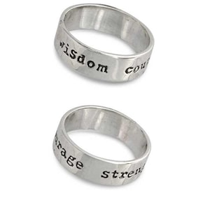 Könnte beinhalten: Zwei silberne Ringe mit gravierten Worten. Der obere Ring sagt "wisdom courage" und der untere Ring sagt "courage strength".