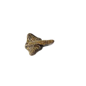 May include: A small, ceramic stingray figurine with a brown and tan glaze. The stingray is in a swimming position with its tail extended.