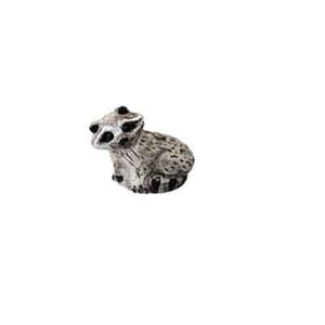 May include: A small, gray and white ceramic raccoon figurine. The raccoon is sitting with its paws tucked under its body.
