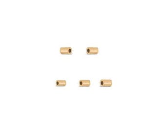 May include: Five small, cylindrical, gold-colored beads are arranged on a white background. Each bead has a hole running through its center. The beads are evenly spaced, suggesting they are for jewelry making or crafts.