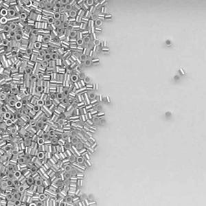 May include: A pile of silver-colored seed beads, with a few beads scattered on a white surface.