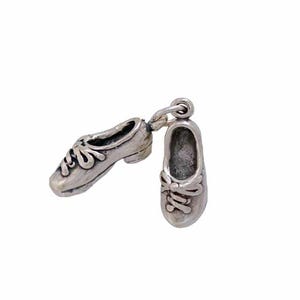 Puede incluir: Un par de zapatos en miniatura de color plateado, posiblemente colgantes o dijes, se muestran sobre un fondo blanco. Los zapatos tienen cordones detallados y una superficie texturizada, conectados por un pequeño lazo.