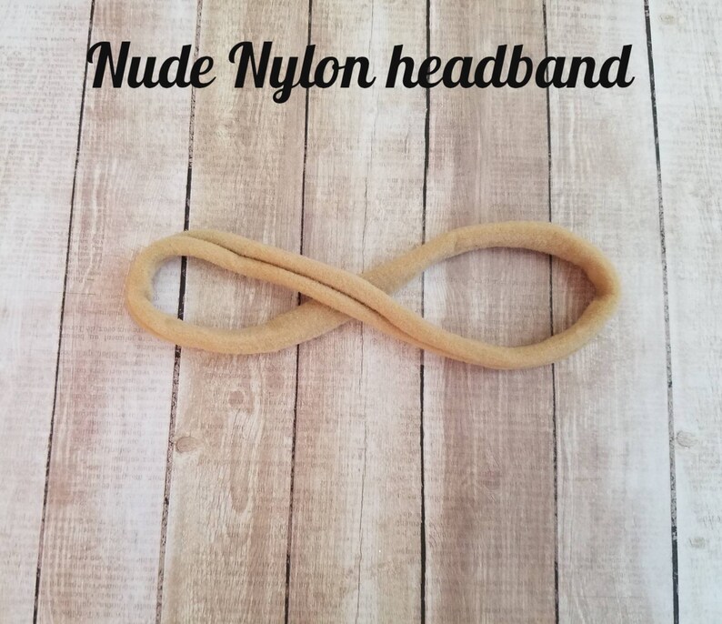 May include: A nude nylon headband, a simple hair accessory, is shown against a light wood background.