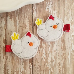 May include: Two white felt chicken hair clips with red and yellow accents. The chickens have closed eyes and are sleeping.