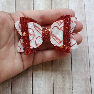 May include: Red glitter hair bow with a white baseball and heart pattern.