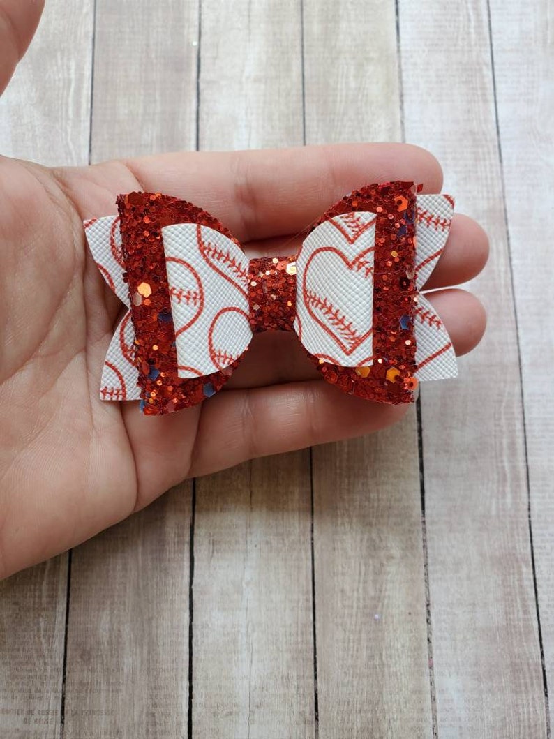 May include: Red glitter hair bow with a white baseball and heart pattern.