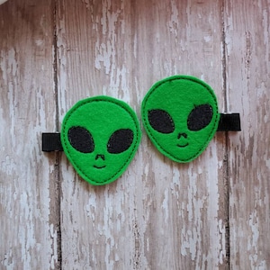 May include: Two green felt alien head hair clips with black felt eyes and mouths. The clips have black elastic bands.