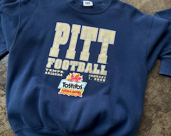 May include: Navy blue sweatshirt with "PITT FOOTBALL" in gold lettering. Features "TEMPE, ARIZONA" and "JANUARY 1, 2005" text. Includes a Tostitos Fiesta Bowl logo. Made by Lee.