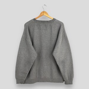 May include: A heather gray sweatshirt hanging on a wooden hanger. The crew neck sweatshirt has long sleeves and a ribbed hem and cuffs. The garment is made of a soft, comfortable material.