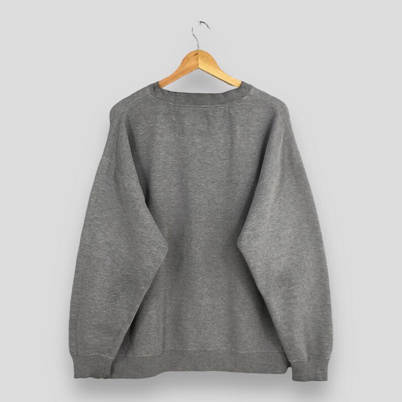 May include: A heather gray sweatshirt hanging on a wooden hanger. The crew neck sweatshirt has long sleeves and a ribbed hem and cuffs. The garment is made of a soft, comfortable material.