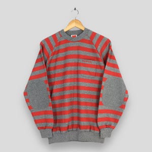 May include: Gray and red striped sweatshirt with elbow patches and a small pocket. The word "HONDA" is embroidered in red on the chest. The sweatshirt is hanging on a wooden hanger.