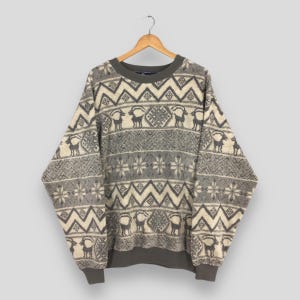 Könnte beinhalten: Ein Vintage-Pullover in Grau und Creme mit geometrischem und Tiermuster. Der Pullover hat einen Rundhalsausschnitt, lange Ärmel sowie gerippte Bündchen und Saum. Das Muster umfasst Zickzackmuster, Hirsche und Schneeflocken.