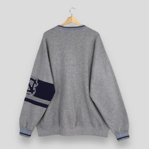 Puede incluir: Una sudadera gris con un dise&ntilde;o azul y marino. La sudadera tiene una franja azul y marino en la manga izquierda y un dise&ntilde;o azul y marino en el pu&ntilde;o. El cuello tiene una franja azul.