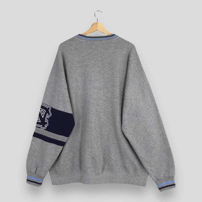 Puede incluir: Una sudadera gris con un dise&ntilde;o azul y marino. La sudadera tiene una franja azul y marino en la manga izquierda y un dise&ntilde;o azul y marino en el pu&ntilde;o. El cuello tiene una franja azul.