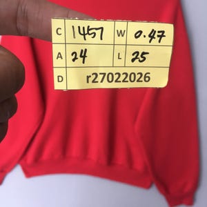 Peut inclure: Un sweat-shirt rouge uni &agrave; manches longues avec une &eacute;tiquette jaune portant le texte C 1457, W 0.47, A 24, L 25 et D r27022026. Le v&ecirc;tement pr&eacute;sente un col rond et des poignets c&ocirc;tel&eacute;s, avec un tissu rouge vif sur toute la surface visible.