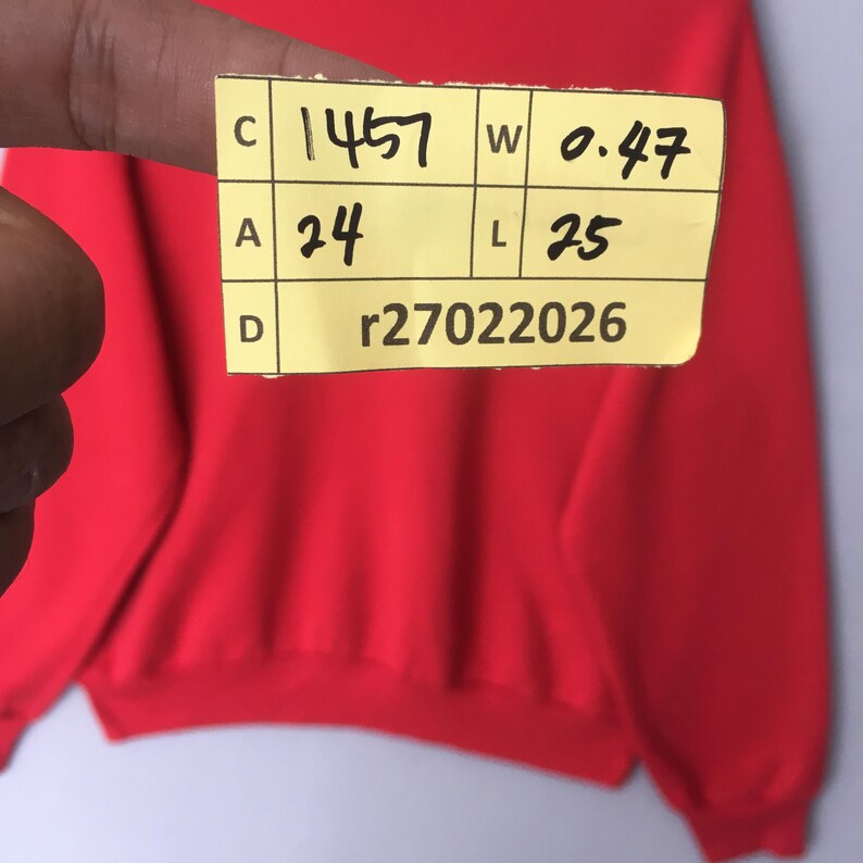 Peut inclure: Un sweat-shirt rouge uni &agrave; manches longues avec une &eacute;tiquette jaune portant le texte C 1457, W 0.47, A 24, L 25 et D r27022026. Le v&ecirc;tement pr&eacute;sente un col rond et des poignets c&ocirc;tel&eacute;s, avec un tissu rouge vif sur toute la surface visible.