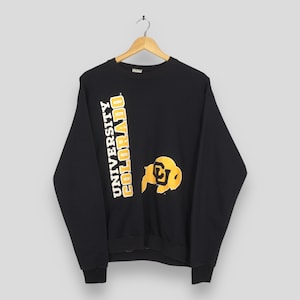 May include: Black crew neck sweatshirt with the words "UNIVERSITY COLORADO" printed vertically in white and gold. A gold and black logo is on the front. The sweatshirt is hanging on a wooden hanger.