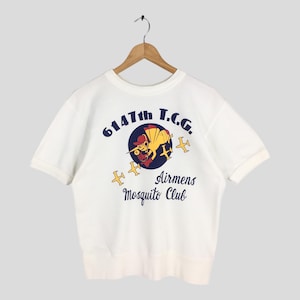 May include: White short-sleeved t-shirt with a graphic on the front. The graphic features a cartoon mosquito in a pilot's hat and goggles, surrounded by text that reads "6147th T.C.G. Airmens Mosquito Club."