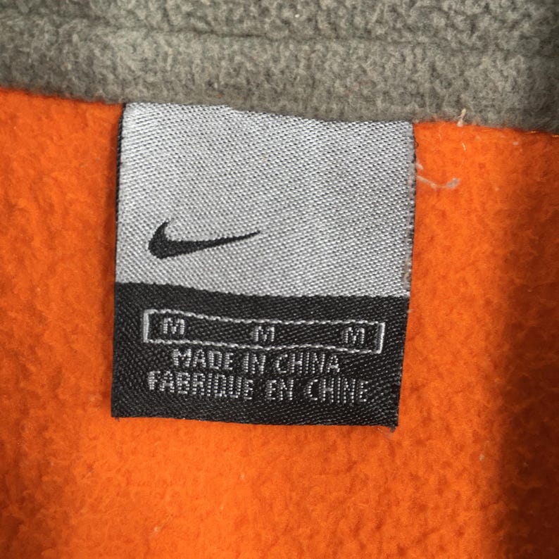May include: A close-up of a Nike clothing label. The label is rectangular with a black background and white text that reads "MADE IN CHINA FABRIQUE EN CHINE". The Nike swoosh logo is visible above the text.