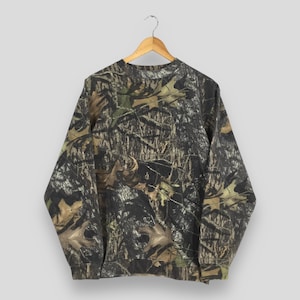 Könnte beinhalten: Ein Sweatshirt mit Camouflage-Muster hängt an einem Holzbügel. Das langärmlige Shirt hat ein braunes, grünes und schwarzes Wald-Camouflage-Design. Das Sweatshirt ist aus weichem Material und hat einen Rundhalsausschnitt.