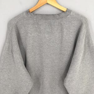 May include: A heather gray sweatshirt with a crew neck, hanging on a wooden hanger. The sweatshirt has long sleeves and a relaxed fit. The fabric appears to be a soft, comfortable material.