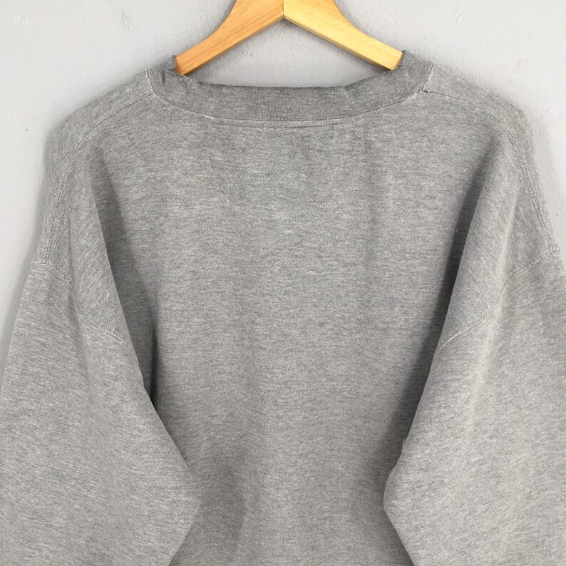 May include: A heather gray sweatshirt with a crew neck, hanging on a wooden hanger. The sweatshirt has long sleeves and a relaxed fit. The fabric appears to be a soft, comfortable material.