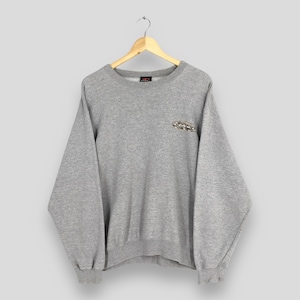 May include: A heather gray sweatshirt with long sleeves, a crew neck, and ribbed cuffs and hem. The sweatshirt has a small embroidered design on the chest. The garment is hanging on a wooden hanger against a light gray background.