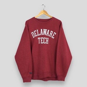 May include: A maroon sweatshirt with the text "DELAWARE TECH" in white, arched lettering. The sweatshirt is hanging on a wooden hanger. The sleeves are long and the cuffs and hem are ribbed.