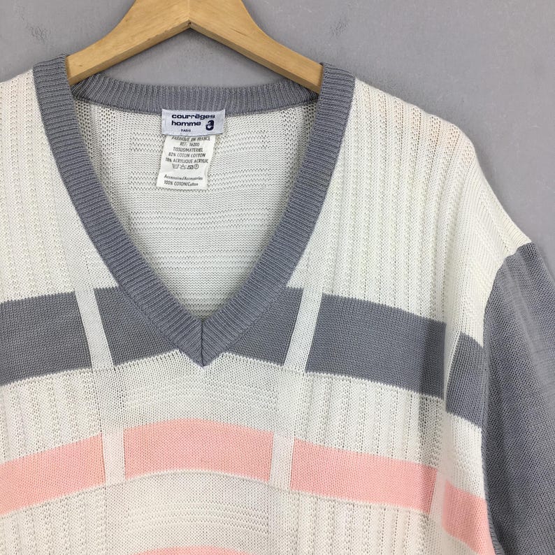 May include: A vintage V-neck sweater in white, gray, and pink. The sweater features a geometric design with gray sleeves and trim. The label reads "courr&egrave;ges homme".