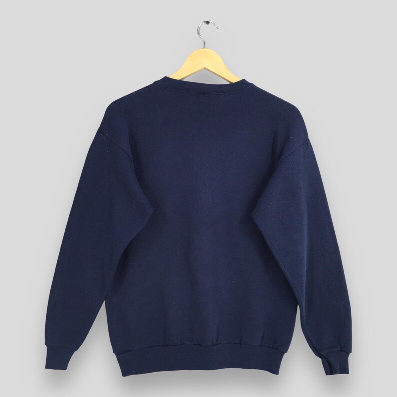 May include: Navy blue sweatshirt with a crew neck and long sleeves. The garment is hanging on a wooden hanger against a light gray background. The sweatshirt appears to be made of a soft, comfortable material.