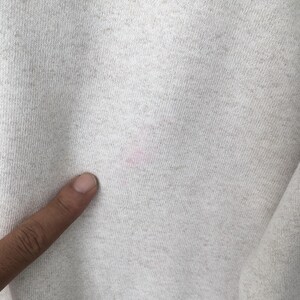 May include: Close-up of a light gray fabric with a textured surface. A pink stain is visible on the fabric. A finger is touching the fabric.