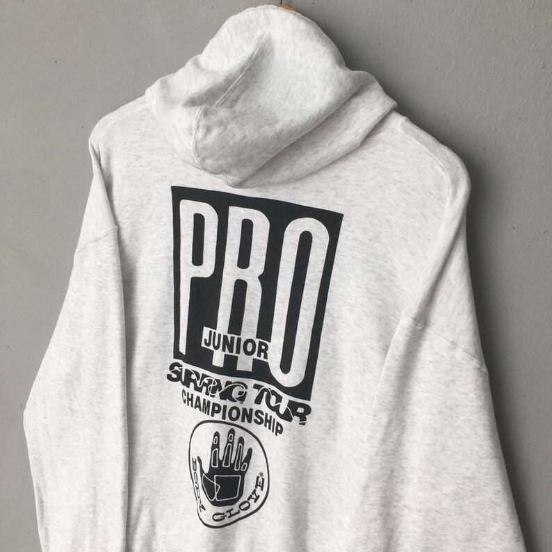 Puede incluir: Una sudadera con capucha gris claro con una capucha y un gran gr&aacute;fico negro en la espalda. El gr&aacute;fico dice "PRO JUNIOR SPRING TOUR CHAMPIONSHIP" con un logotipo de mano. La sudadera con capucha est&aacute; hecha de un material suave y c&oacute;modo.