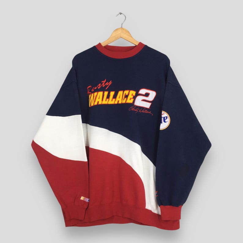 May include: A vintage crew neck sweatshirt in navy, white, and red, featuring "Rusty Wallace 2" in yellow and white lettering. The long-sleeved top has a color block design and a small patch on the sleeve.