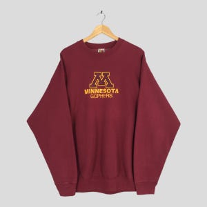 May include: Maroon sweatshirt with the text "MINNESOTA GOPHERS" in gold lettering. The sweatshirt has a crew neck and long sleeves. The logo is centered on the chest.