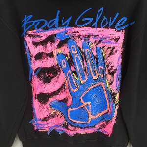 May include: Black sweatshirt with a vibrant graphic featuring a blue handprint within a pink and blue rectangular design. The words "Body Glove" are written above the handprint in blue. The sweatshirt is a casual apparel item.
