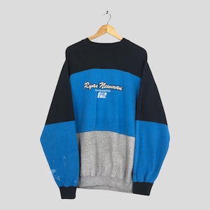 May include: A vintage crew neck sweatshirt in black, blue, and gray color block design. The sweatshirt features the name "Ryan Newman" in white script above the number "12" in blue. The sleeves are black, and the body is blue and gray.