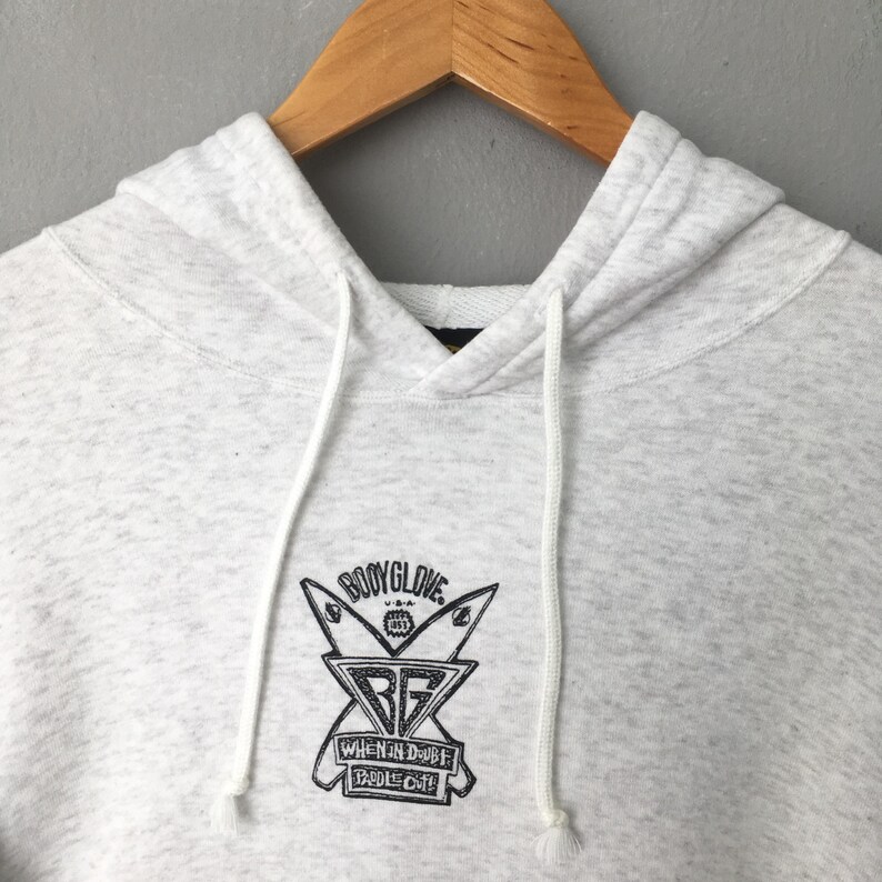 Puede incluir: Una sudadera con capucha gris claro con capucha con cord&oacute;n y bolsillo de canguro. La parte delantera presenta un gr&aacute;fico negro del logotipo de Body Glove y el texto "WHEN IN DOUBT PADDLE OUT". La sudadera con capucha est&aacute; hecha de un material suave y c&oacute;modo.