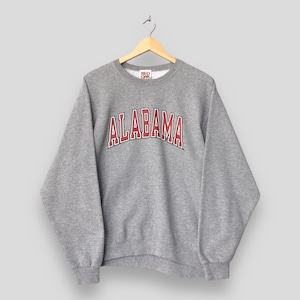 May include: A gray sweatshirt with the word "ALABAMA" in red and white lettering across the chest. The sweatshirt is hanging on a wooden hanger against a neutral background. The Red Oak brand tag is visible.